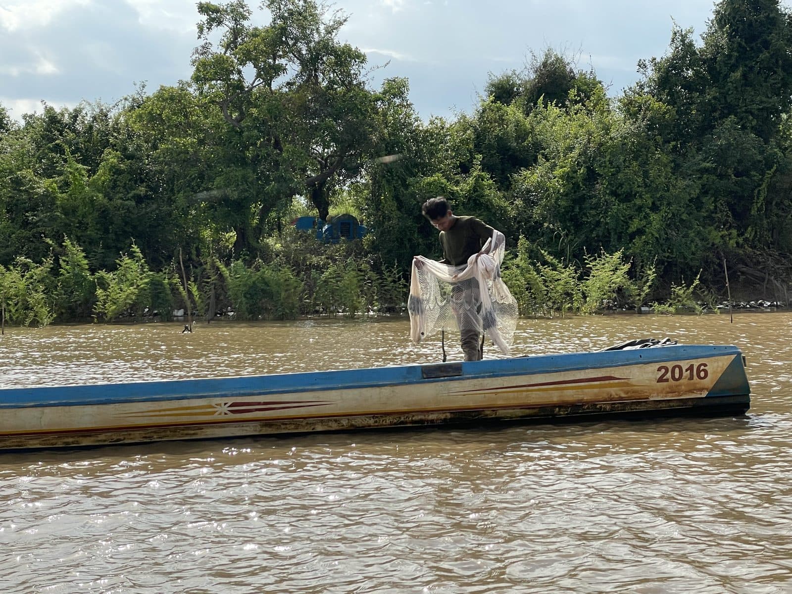 A fisherman gathering his net on a boat on a Cambodian river