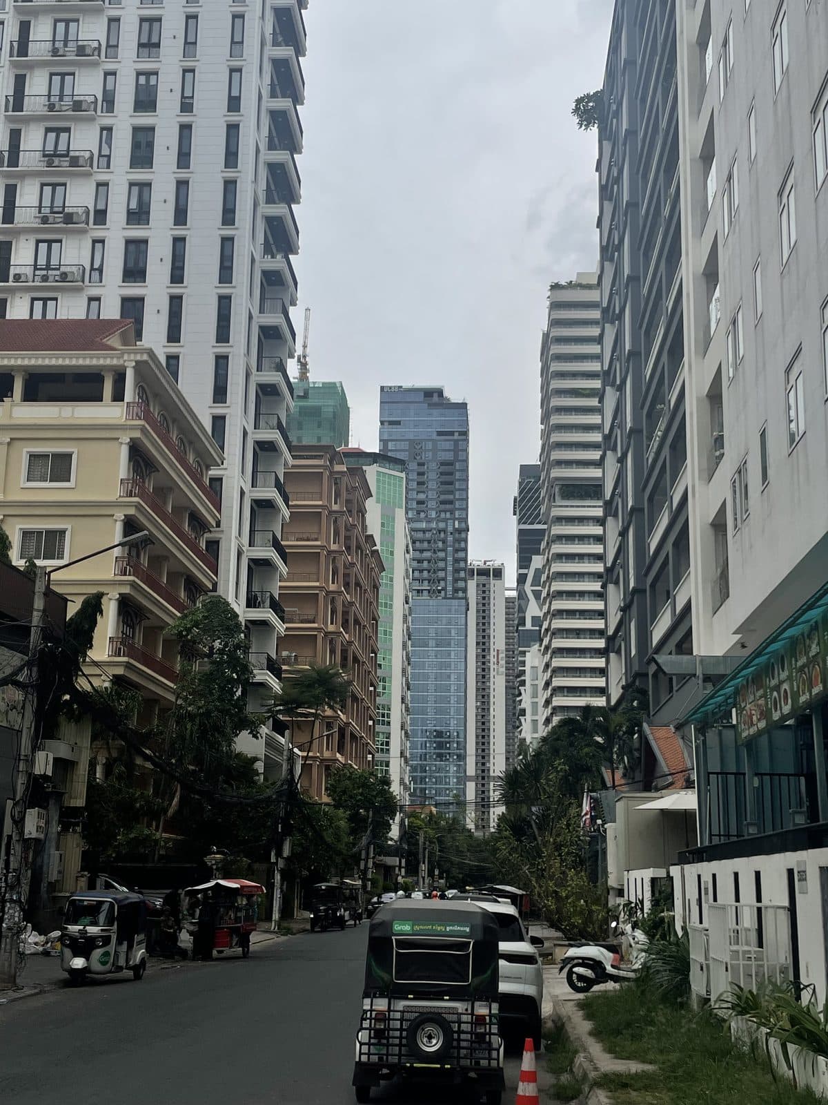 A quiet Phnom Penh street lined with apartment buildings, a tuk-tuk parked at the curb